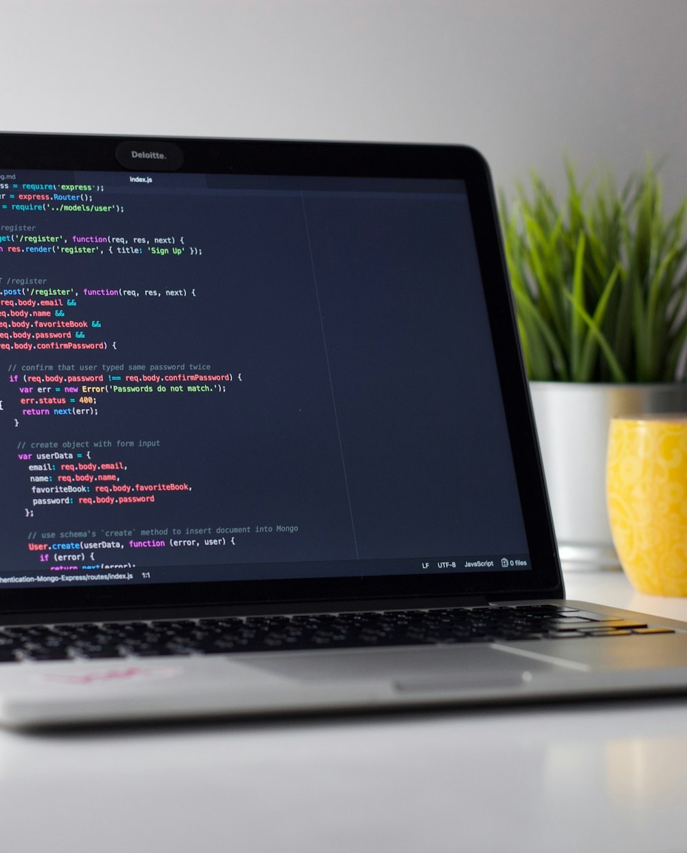A laptop at night showing a dark-mode code editor, next to a small plant and a mug on a desk